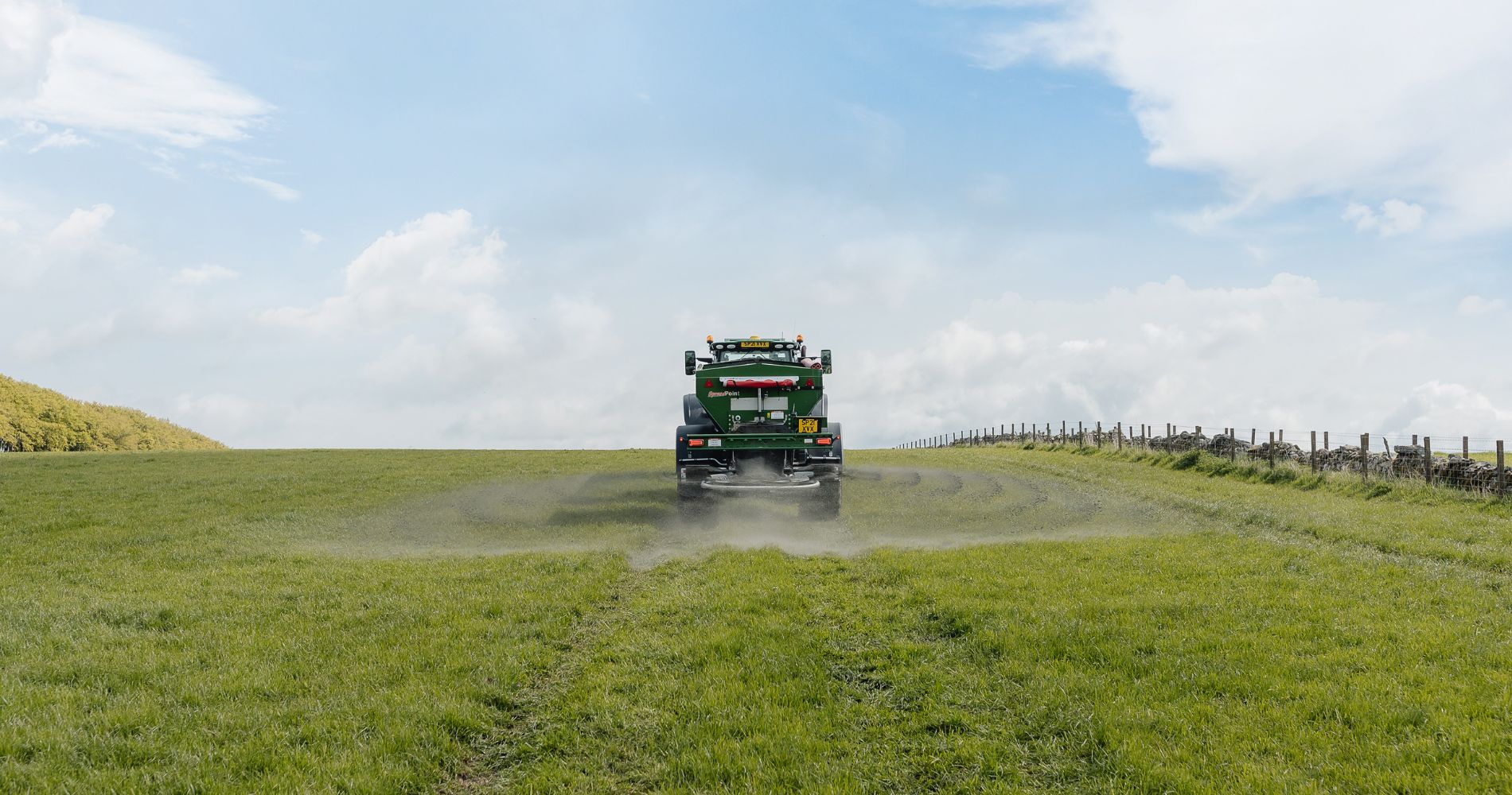 A tractor spreading a layer of crushed basalt across a grassy field under a blue sky, illustrating enhanced rock weathering, a process for carbon removal and soil enrichment.